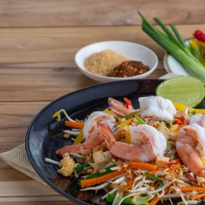 Pad Thai, fresh shrimp in a black dish, placed on a wooden table.